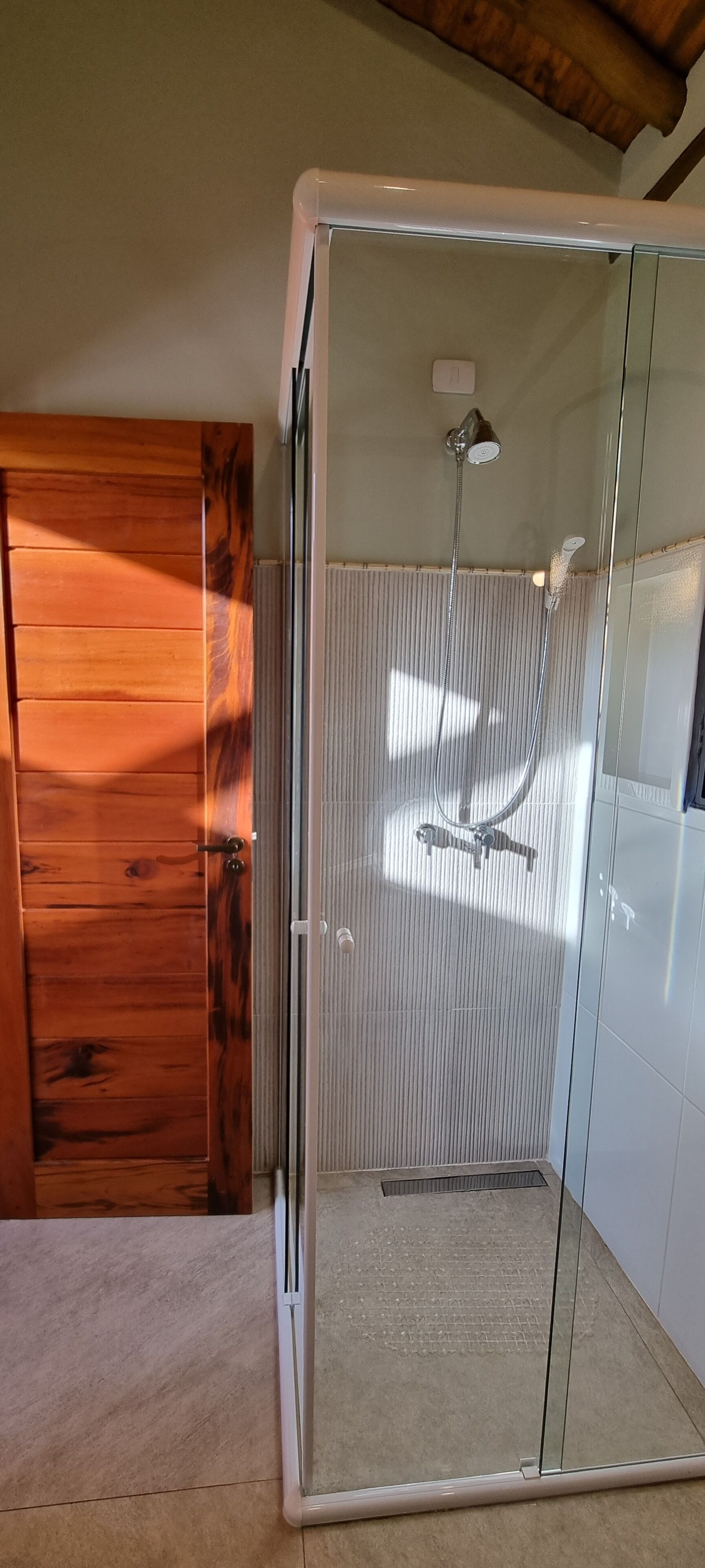 A glass-enclosed shower with a handheld showerhead and a wall-mounted faucet.