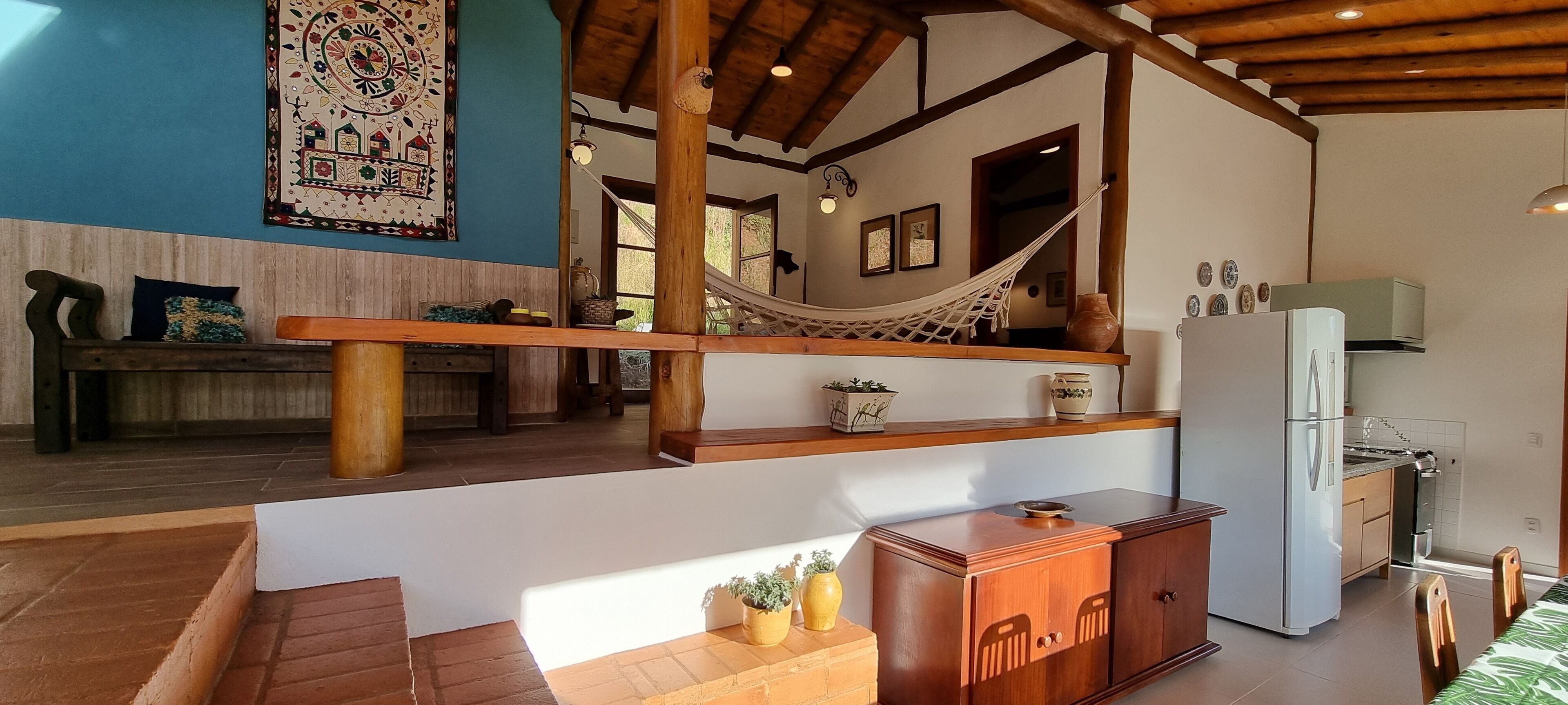Un salón amplio con una hamaca, muebles de madera, un refrigerador y una zona de cocina.
