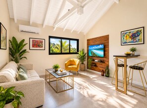 A modern living room with a sofa, a yellow armchair, a coffee table, and a TV mounted on a wooden wall. - The Forest Suites at Anse Marcel | Boutique Hotel & Restaurant (Anse Marcel)