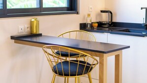 A compact kitchen with a black countertop, gold chairs, and a window with a view of greenery. - The Forest Suites at Anse Marcel | Boutique Hotel & Restaurant (Anse Marcel)