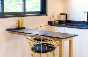 A compact kitchen with a black countertop, gold chairs, and a window with a view of greenery. - The Forest Suites at Anse Marcel | Boutique Hotel & Restaurant (Anse Marcel)