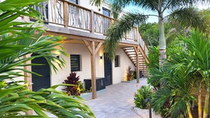 Un edificio con balcón de madera, un sendero adoquinado y diversas plantas tropicales.