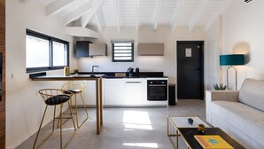 A modern kitchen with a central island, bar stools, a dining table, and a sofa in a bright living area with a high ceiling and skylights. - The Forest Suites at Anse Marcel | Boutique Hotel & Restaurant (Anse Marcel)