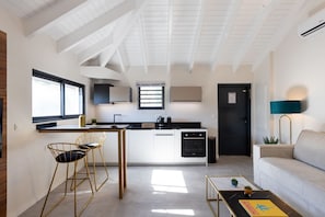 A modern kitchen with a central island, bar stools, a dining table, and a sofa in a bright living area with a high ceiling and skylights. - The Forest Suites at Anse Marcel | Boutique Hotel & Restaurant (Anse Marcel)