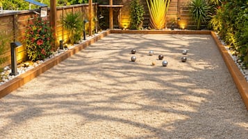 An outdoor bocce court with a wooden frame, surrounded by plants and a decorative canopy.