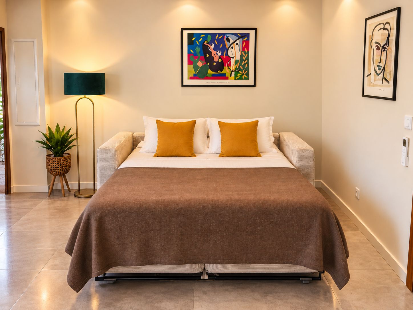 Une chambre à coucher comprenant un lit, deux oreillers, une lampe de sol et deux œuvres d’art accrochées au mur.
