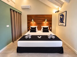 Una cama doble con cabecera de madera, dos lámparas de noche y una obra enmarcada en la pared.