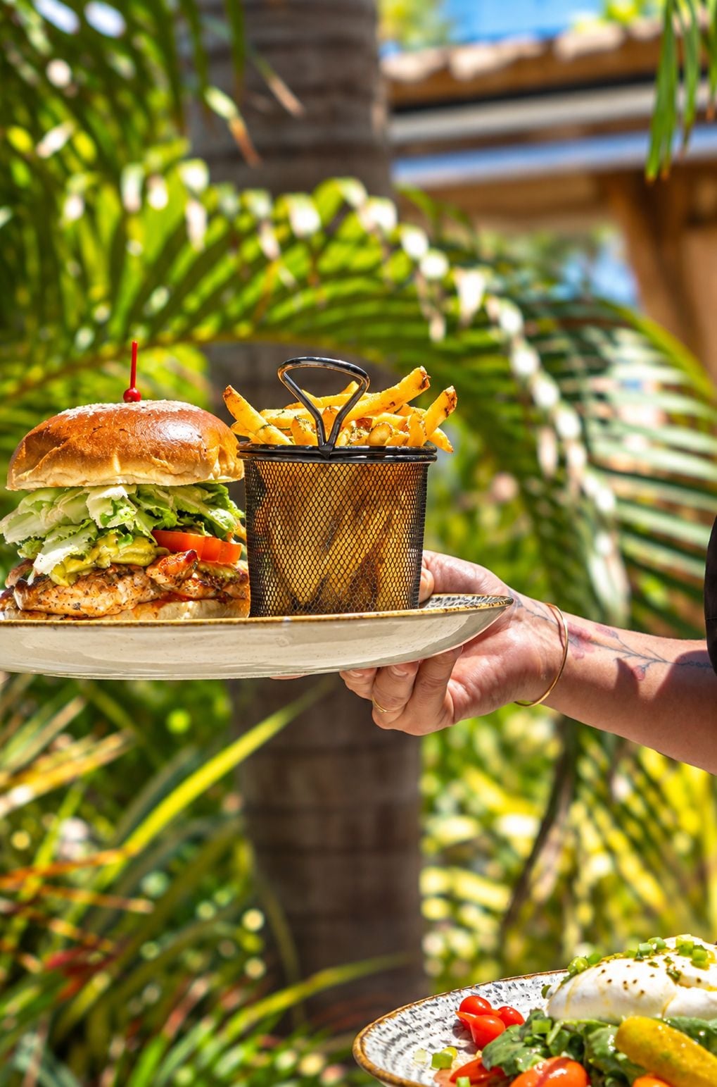 A person holding a plate with a burger and fries, and a small bowl of salad.