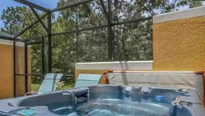 Ein Whirlpool mit Holzterrasse und Glasumrandung, umgeben von Bäumen.