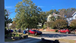 Une rue résidentielle bordée de maisons, de voitures garées et d’un arbre.