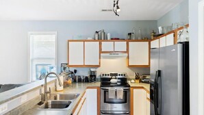 Une cuisine moderne dotée d’appareils électroménagers en acier inoxydable, de meubles en bois et d’une fenêtre avec des stores.