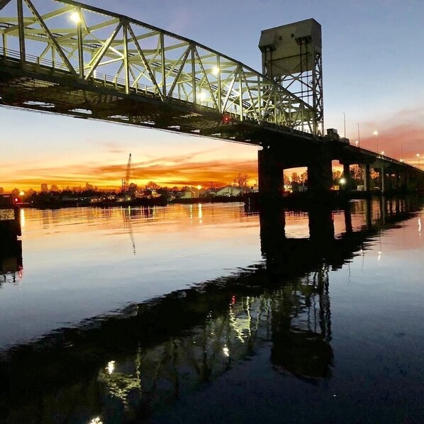 A steel bridge over a calm river at sunset with city lights in the background.