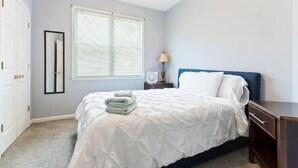 Une chambre à coucher avec un lit, une table de chevet, une lampe et une fenêtre avec des stores.