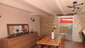 Ein Essbereich mit Holztisch und -stühlen, einer Steinwand und einer durch einen offenen Durchgang erkennbaren Küche.