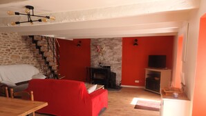 Ein Wohnzimmer mit rotem Sofa, Holzboden, Kamin, Fernseher und einer Treppe.
