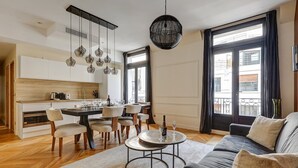 Un salon moderne comprenant un canapé, une table à manger avec des chaises, un coin cuisine et de grandes fenêtres avec des rideaux.