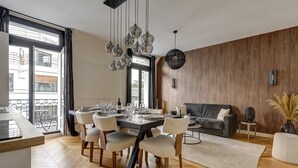 Un espace de salle à manger moderne avec un parquet en bois disposé en chevrons, une table à manger entourée de chaises et un mur d’accent en bois foncé.