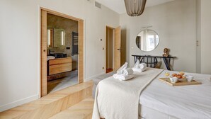 Une chambre d’hôtel moderne avec un grand lit, une coiffeuse en bois, un miroir et un plateau de petit-déjeuner posé sur le lit.