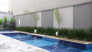 Piscina rectangular con azulejos azules, rodeada por un muro bajo y plantas verdes.