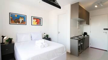Een moderne hotelkamer met een groot bed, een klein bureau, een kitchenette en twee ingelijste kunstwerken aan de muur.