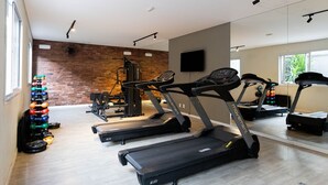 Un gimnasio con cintas de correr, máquinas de pesas y una pared de ladrillo.