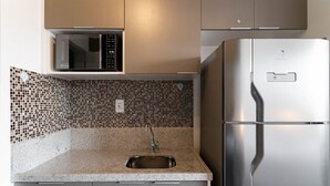 Una cocina con refrigerador de acero inoxidable, microondas y pileta con salpicadero de azulejos.