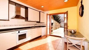 A kitchen with white cabinets, a stove, and a sink. There is a window with a view of a stone wall and trees. - House 4 rooms 10 Pax, Fireplace, BBQ & Cadí Views (Montellà)