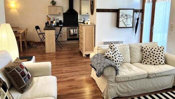 A living room with a sofa, a dining area with a table and chairs, a kitchen with cabinets and a stove, and a window with curtains.