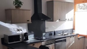 A modern kitchen with a black range hood, stainless steel appliances, and wooden cabinets.