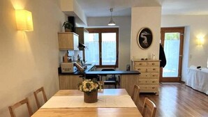 A dining area with a wooden table and chairs, a vase of flowers, and a view of the kitchen and living area.