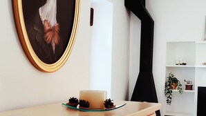 A modern room with a framed artwork of a bird, a wooden table with a candle and pine cones, and a black abstract sculpture.