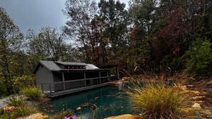 Una cabaña con un muelle que se extiende sobre un lago, rodeada de árboles y piedras.