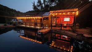 Una cabaña de madera con un muelle que se adentra en un lago tranquilo, rodeada de árboles.