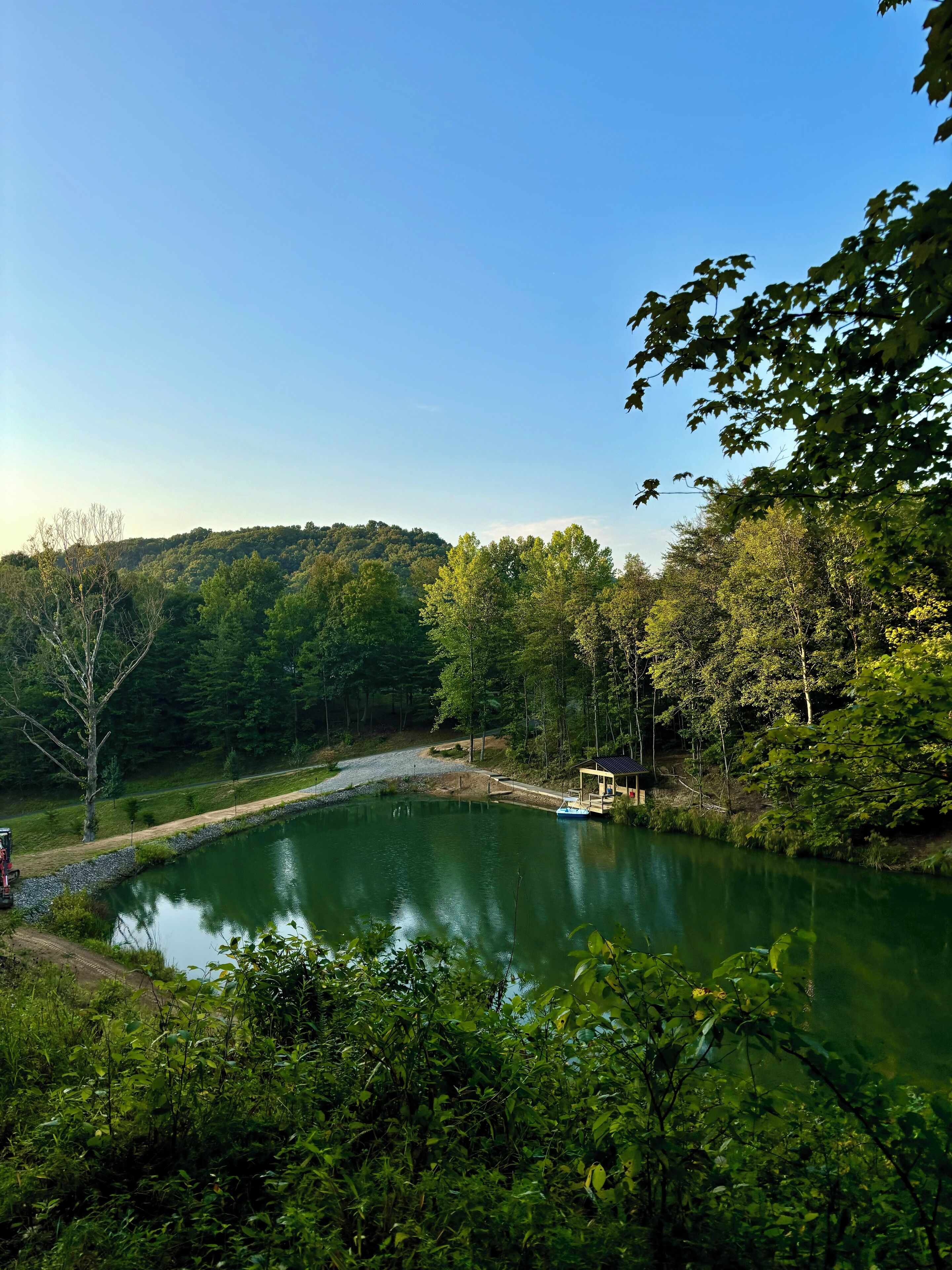 A serene lake surrounded by dense forest, a dock with a boat, and a small building with a roof.