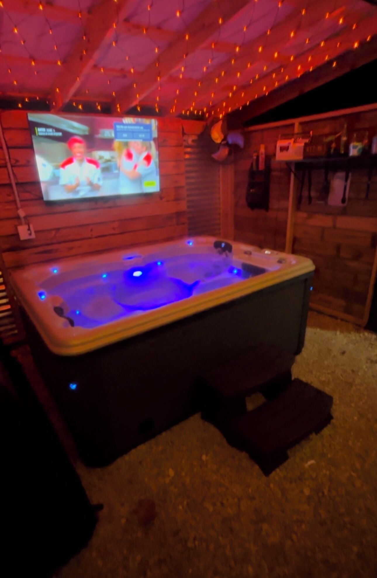 Een jacuzzi met blauwe LED-verlichting, een aan de muur bevestigde televisie en houten lambrisering.
