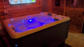 Een jacuzzi met blauwe LED-verlichting, een aan de muur bevestigde televisie en houten lambrisering.