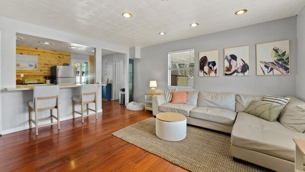 A modern living room with a sofa, a coffee table, and a kitchen area with a refrigerator and bar stools. - 10 min Lido Key Beach~St. Armand Circle~ Short drive to Siesta Key Beach (Sarasota)