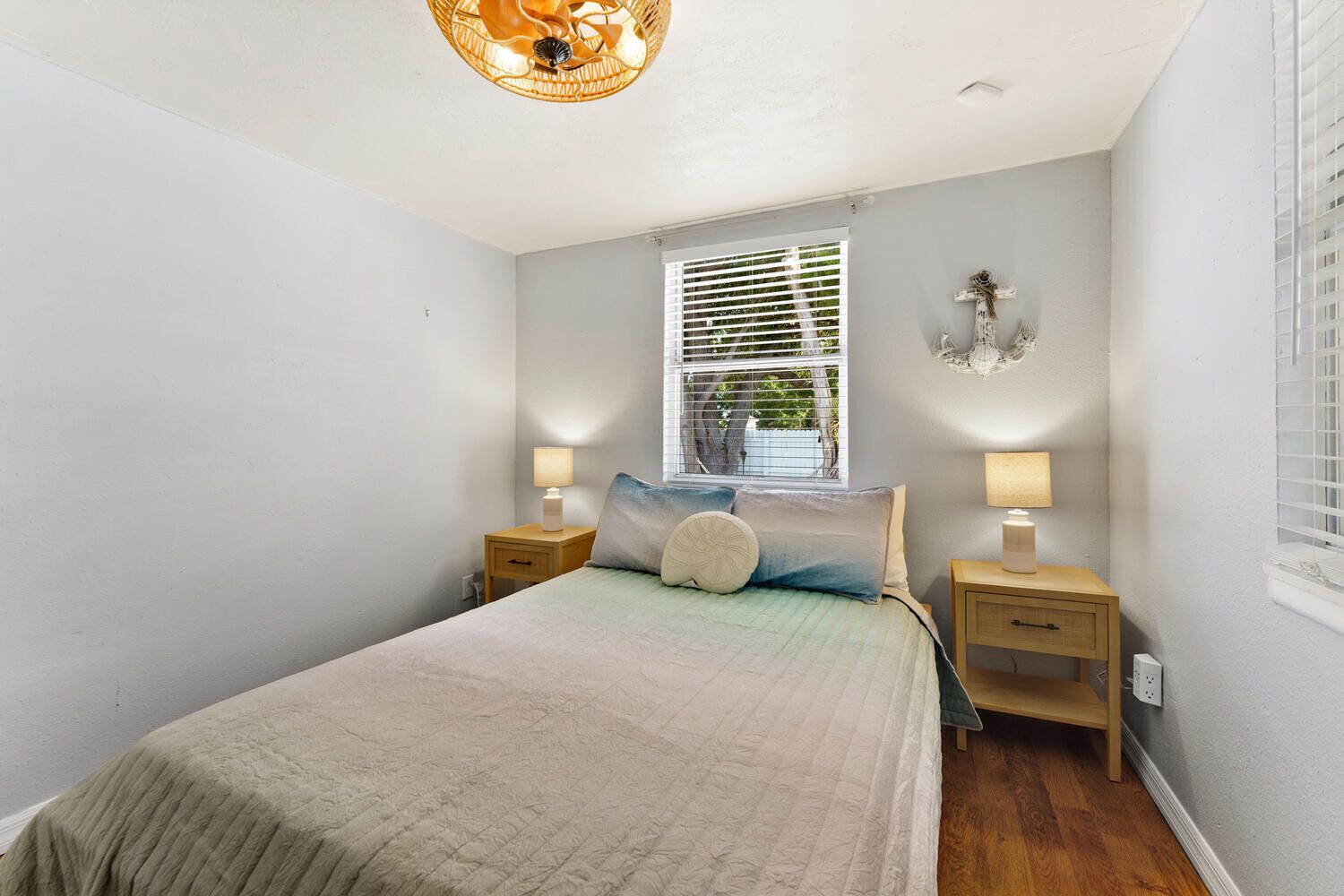 Quarto com cama, duas mesas de cabeceira com abajures, janela com persianas e luminária na parede.