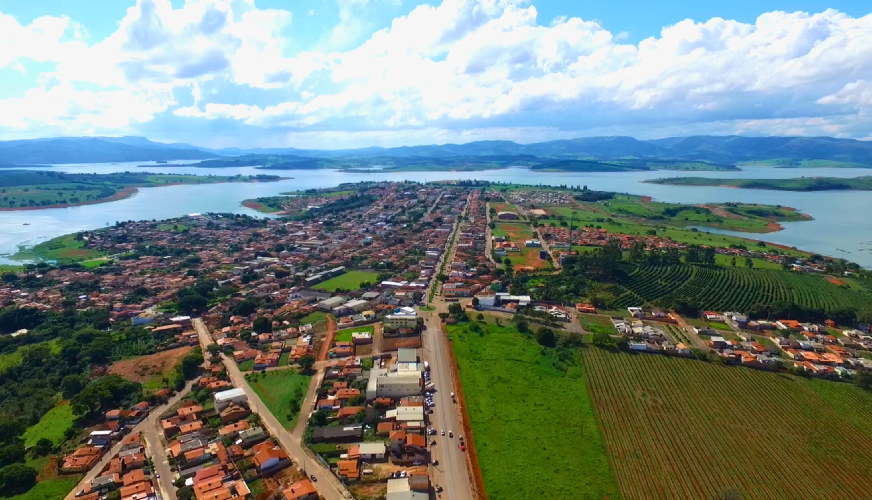 Vista aerea di una cittadina costiera con un fiume, campi verdi e un mix di edifici residenziali e commerciali.