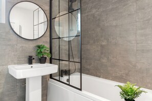 Une salle de bain moderne avec un lavabo blanc, un miroir rond et une douche à parois de verre.