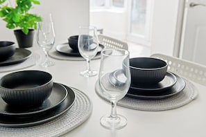 Une table à manger dressée avec des bols noirs, des assiettes et un verre à vin, et une plante en pot en arrière-plan.