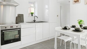 Moderni keittiö, jossa on valkoiset kaapit, sisäänrakennettu uuni ja ikkunalaudalla kasvi.