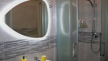 A modern bathroom with a large oval mirror, a sink with two yellow soap dispensers, and a glass-enclosed shower area.