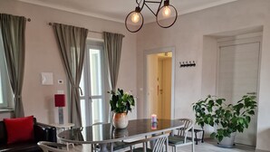 A modern living room with a dining table, chairs, a sofa, and a large window with curtains. - Locanda La Guienda (Torre Canavese)