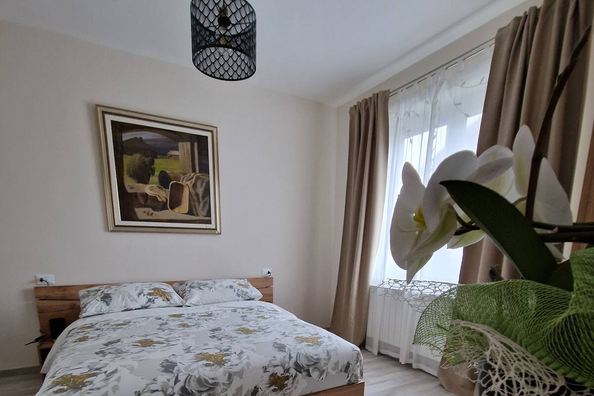 A bedroom with a wooden bed, a hanging light fixture, a framed painting on the wall, and a potted orchid plant.