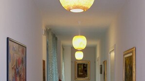 A hallway with wooden flooring, framed artwork on the walls, and a hanging light fixture. - Locanda La Guienda (Torre Canavese)