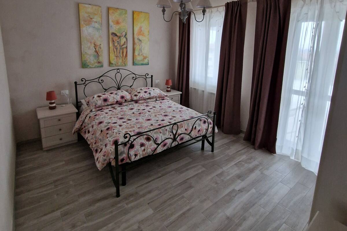 A bedroom with a bed, a nightstand, a lamp, and three paintings on the wall.