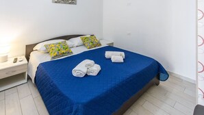 A neatly made bed with a blue bedspread, two pillows with floral patterns, and rolled towels on the bed. - Condoluci Apartment - Tropea (Tropea)
