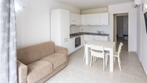 A modern kitchen with white cabinets, a dining table with chairs, and a beige sofa. - Condoluci Apartment - Tropea (Tropea)