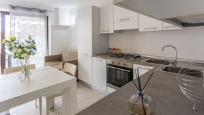 A modern kitchen with white cabinetry, a gas stove, a sink, and a dining area with a table and chairs. - Condoluci Apartment - Tropea (Tropea)